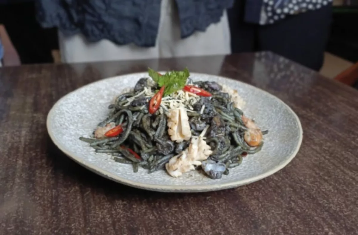 Spaghetti hitam spesial Halloween karya Chef Anton tersaji di atas piring dengan paduan pasta berwarna hitam, potongan seafood, taburan keju, irisan cabai merah, dan hiasan daun hijau. Foto: Wildan-Rizal/Ayojatim